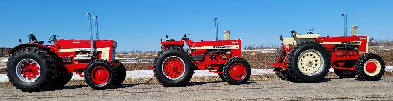 Three red tractors parked on the side of the road.